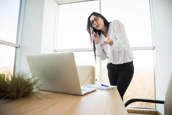 Mujer de negocios hablar por teléfono y mirar el ordenador portátil en su oficina . — Foto de Stock