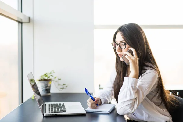 Ung kvinna arbetare sitter på kontor med telefon. — Stockfoto