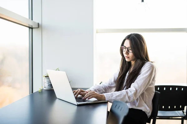 Femeie tânără lucrător care stă în birou în timp ce utilizează computerul laptop și tastează după tastatură — Fotografie, imagine de stoc