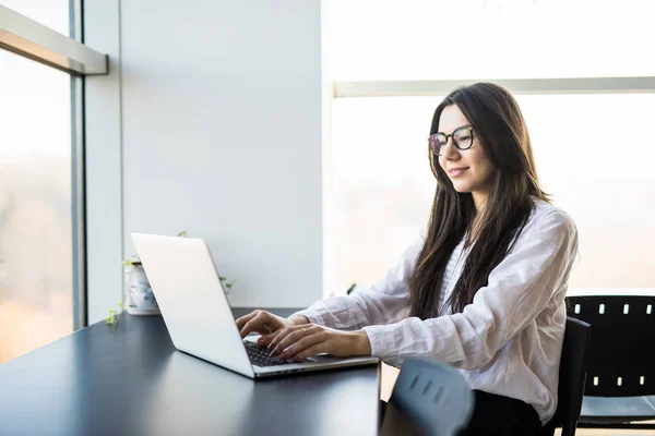 Joven mujer trabajadora sentada en la oficina mientras usa el ordenador portátil y escribe por teclado —  Fotos de Stock