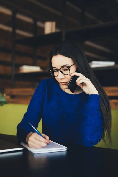 Business lady speak on phone and make notes at work table in office hub