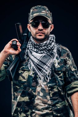 Terrorist atack. Portrait of Terrorist with gun and sunglases over dark background clipart