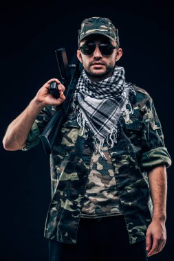 Terrorist atack. Portrait of Terrorist with gun and sunglases over dark background clipart