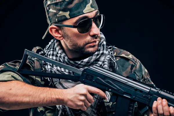 Ataque terrorista. Retrato de Terrorista com arma e óculos de sol sobre fundo escuro — Fotografia de Stock