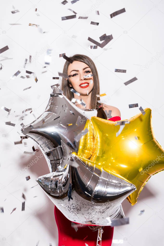 Young woman in red dress holding star balloon with fly confetti at party