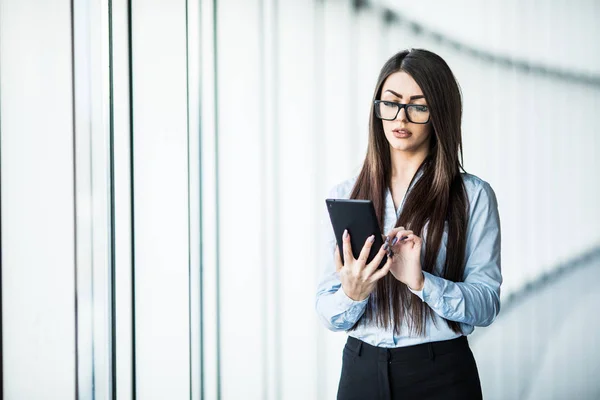 Señora de negocios utilizar la tableta digital cerca de ventanas panorámicas en la oficina moderna . — Foto de Stock