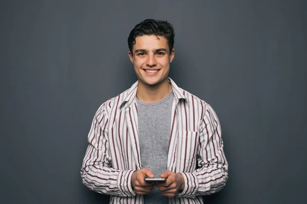 適切な言葉を選択します。灰色の背景に坐っている間携帯電話を保持しているハンサムな若い男 — ストック写真