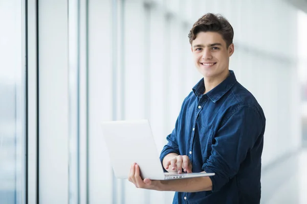 Hombre joven guapo sosteniendo una computadora portátil en el pasillo —  Fotos de Stock