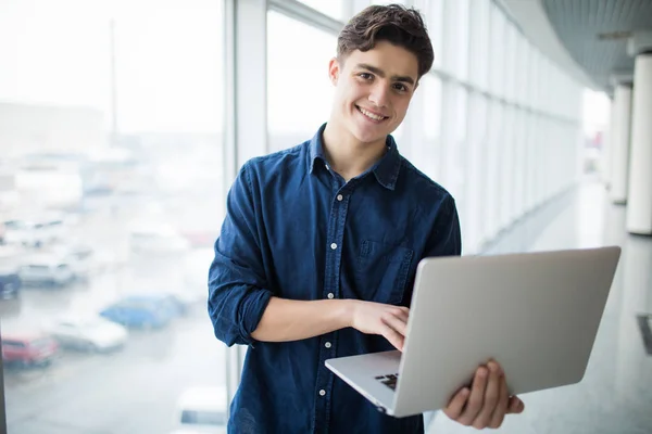 Hombre joven guapo sosteniendo una computadora portátil en el pasillo —  Fotos de Stock