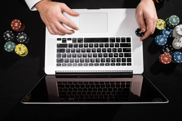 Mãos do jogador online com laptop na vista superior da mesa verde, ele está ganhando e levando todas as fichas — Fotografia de Stock