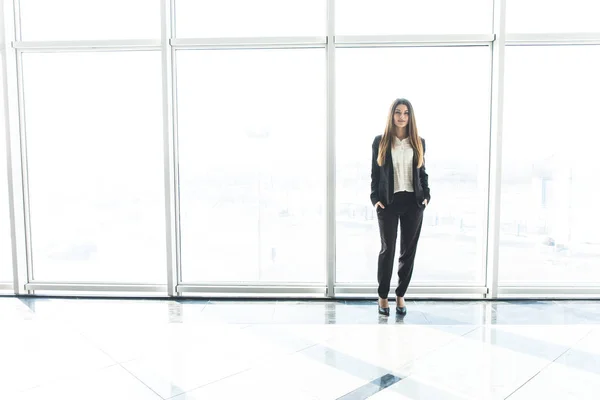 Молода бізнес-леді стоїть в офісі проти панорамних вікон — стокове фото