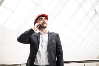 Blueprint tutarak ve duran cep telefonu konuşurken hardhat yakışıklı genç adam