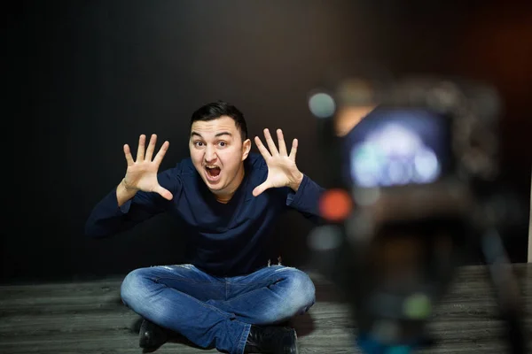 Νεαρός άνδρας στην εστίαση στην ψηφιακή φωτογραφική μηχανή οθόνη κουνώντας το χέρι ενώ κάθεται στο έδαφος τοίχο για αντίληψη σχετικά με το blogging βίντεο — Φωτογραφία Αρχείου