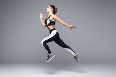 Sportif bir genç kadın atlama gri arka plan üzerinde izole yan görünüm