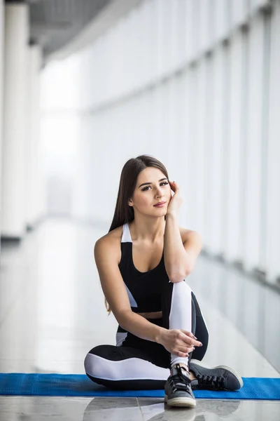 Mujer atlética joven está sentado relajante, descansando entre entrenamientos cerca de ventanas panorámicas en el gimnasio — Foto de Stock