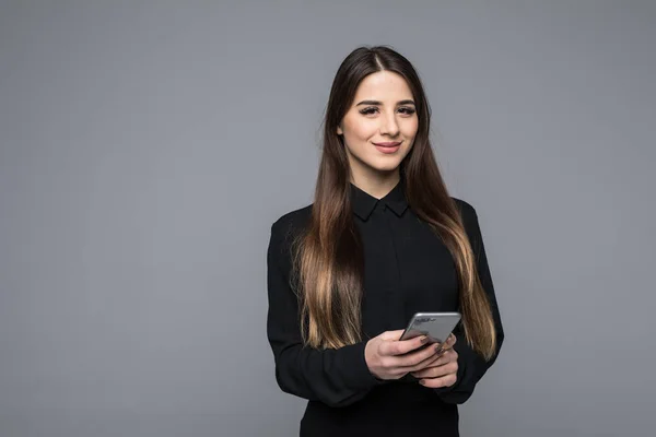 Bella giovane donna d'affari in possesso di telefono cellulare e guardando la fotocamera mentre in piedi sullo sfondo grigio — Foto Stock
