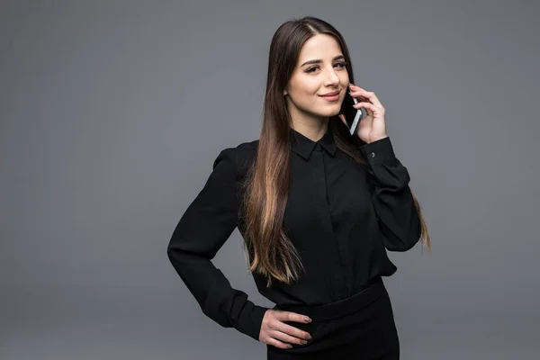 Mujer joven de confianza hablando en el teléfono móvil mientras está de pie sobre un fondo gris —  Fotos de Stock