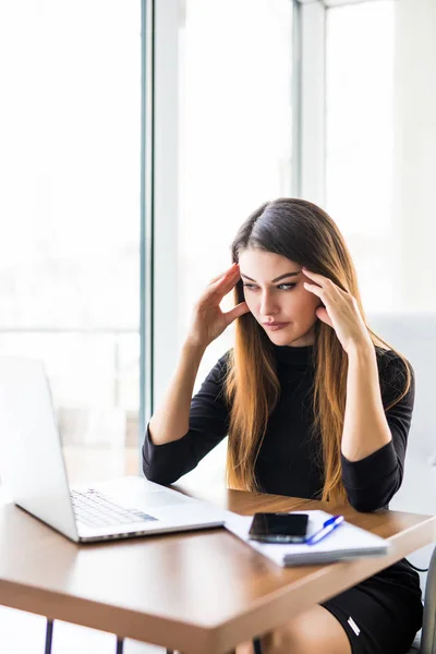 Young attractive woman at modern office desk, working on laptop, massaging temples to forget about constant headaches, noisy loud office giving a migraine, relieving stress, chronic pain, help soothe — Stock Photo, Image