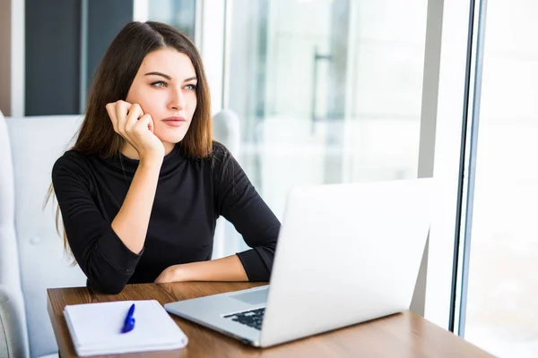 Mujer joven aburrida en la oficina trabajando con un ordenador portátil — Foto de Stock