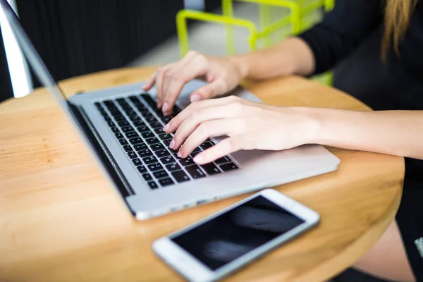 Manos femeninas escribiendo en el teclado de la computadora, teléfono en la mesa — Foto de Stock