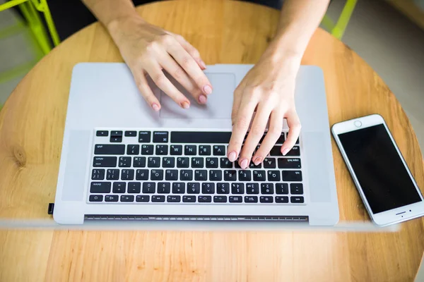 Manos femeninas escribiendo en el teclado de la computadora y el teléfono desde arriba — Foto de Stock