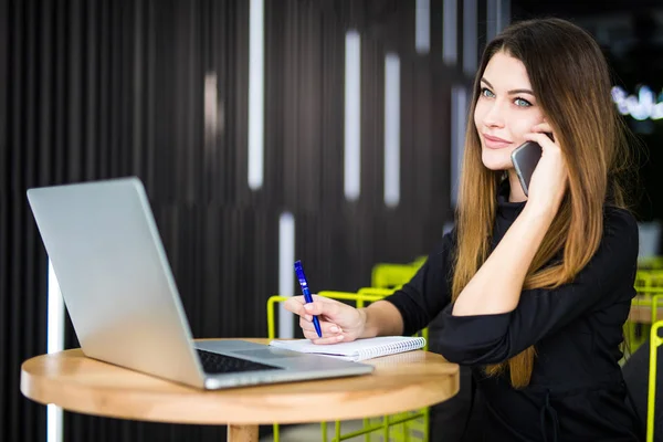 Feliz bastante gerente hablando en el teléfono móvil con el cliente y escribir notas en la oficina moderna — Foto de Stock