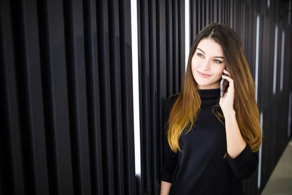 Portret van een jonge vrouw praten op mobiele telefoon tegen moderne kantoor muur — Stockfoto