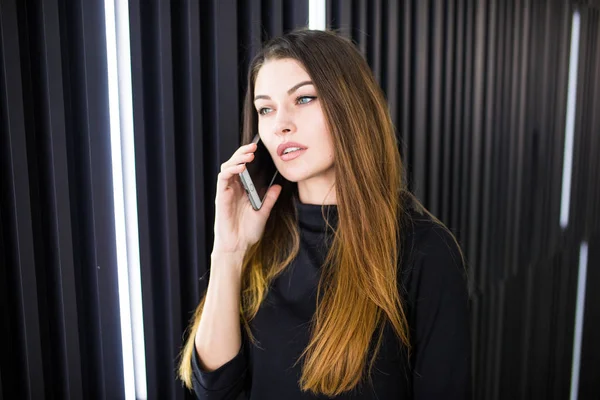 Egy fiatal nő, mozgatható telefon, korszerű falnak beszél portréja — Stock Fotó