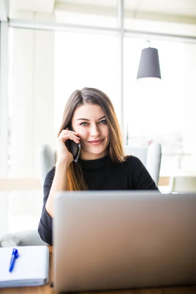 Mujer sonriente independiente sentada en la cafetería con portátil y teléfono móvil — Foto de Stock