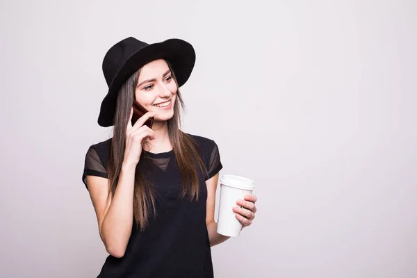 Egy mosoly kalap, mozgatható telefon és kávét egy szürke elszigetelt fiatal lány portréja — Stock Fotó