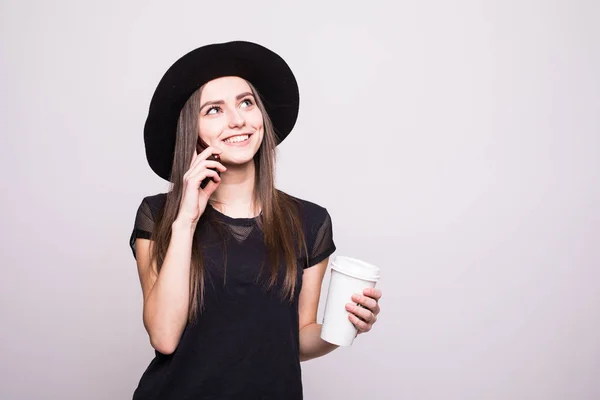 Egy mosoly kalap, mozgatható telefon és kávét egy szürke elszigetelt fiatal lány portréja — Stock Fotó