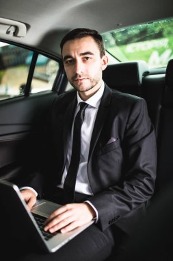 Yakışıklı genç işadamı üzerinde diz üstü arabada otururken kameraya bak