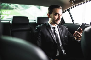 Akıllı telefonunu ayarlama ve arabada otururken kameraya bakarak kendine güvenen genç işadamı