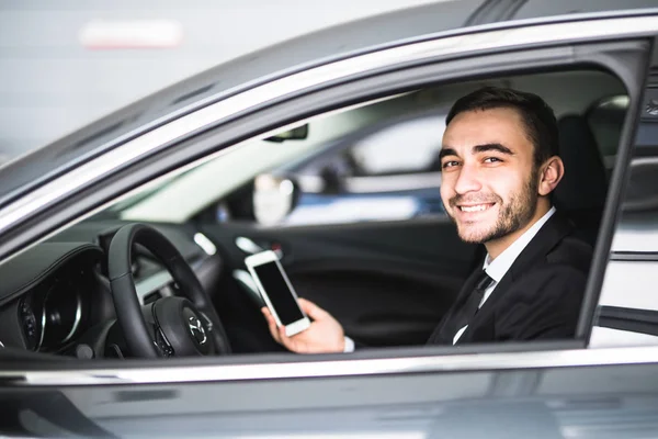 Бизнесмен в машине использует смартфон и улыбается на камеру — стоковое фото