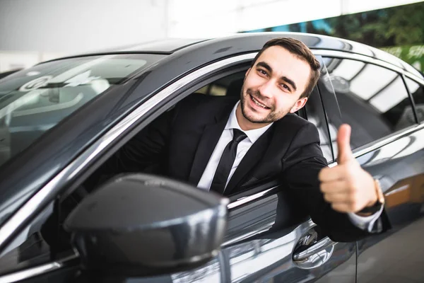 Empresario sonriendo a la cámara mostrando pulgares en su coche — Foto de Stock