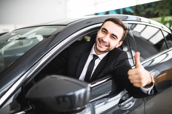 Empresario sonriendo a la cámara mostrando pulgares en su coche — Foto de Stock