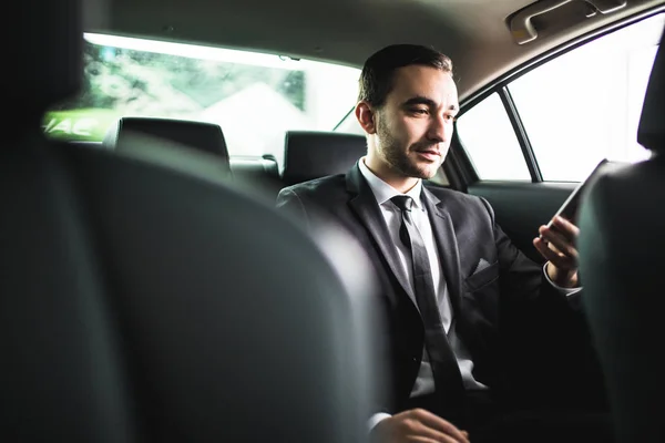 Selbstbewusster junger Geschäftsmann, der sein Smartphone einsetzt und im Auto in die Kamera schaut — Stockfoto