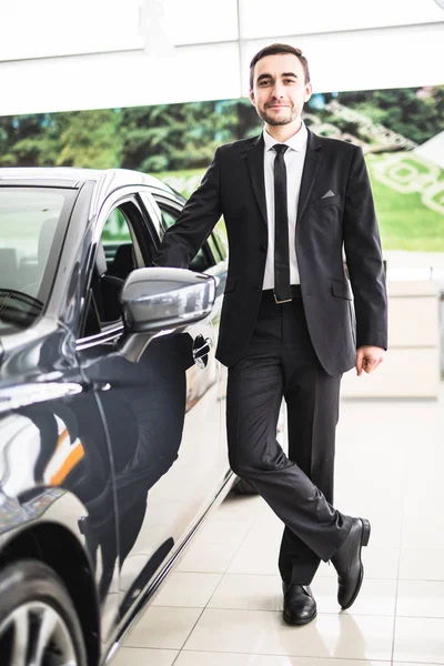 Guapo joven vendedor de coches clásicos de pie en el concesionario — Foto de Stock