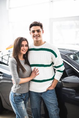 Beautiful young couple standing at the car dealership and making their decision clipart