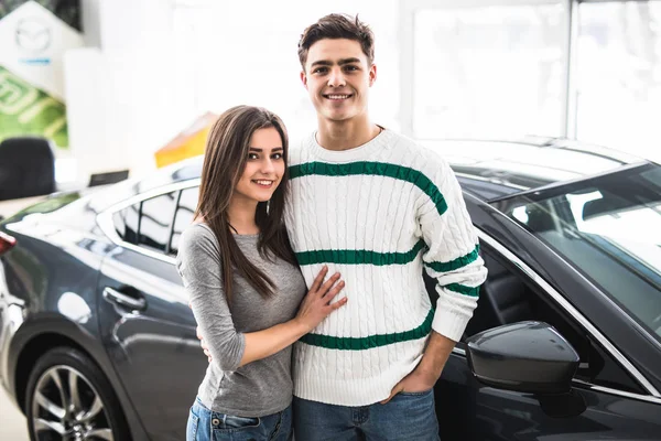 Belo jovem casal de pé na concessionária escolhendo o carro para comprar — Fotografia de Stock