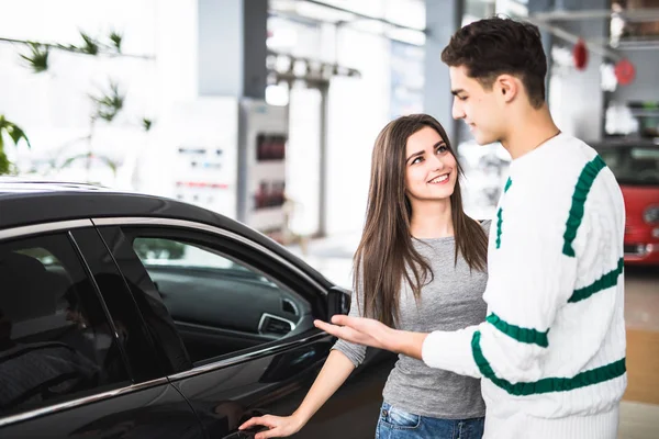 Belo jovem casal de pé na concessionária escolhendo o carro para comprar — Fotografia de Stock