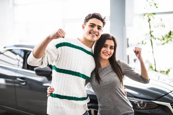 Casal animado comprando um carro no revendedor com os braços para cima — Fotografia de Stock