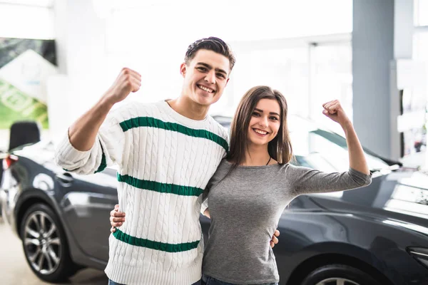 Casal animado comprando um carro no revendedor com os braços para cima — Fotografia de Stock