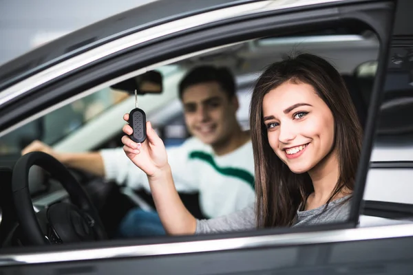 Belo jovem casal sentado nos bancos da frente de seu novo carro, enquanto a mulher mostrando chaves e sorrindo — Fotografia de Stock