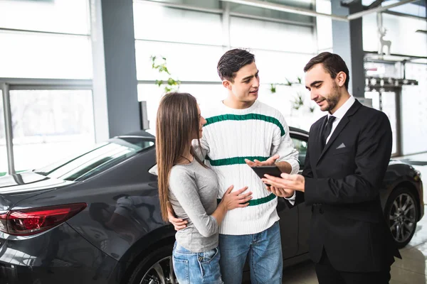 Casal feliz com carro revendedor olhar para tablet em auto show ou salão — Fotografia de Stock