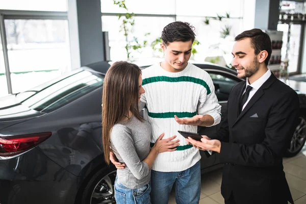 Casal feliz com carro revendedor olhar para tablet em auto show ou salão — Fotografia de Stock