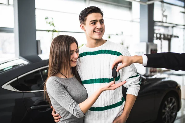 Щаслива пара дивиться на руку продавця, отримуючи ключі від машини — стокове фото