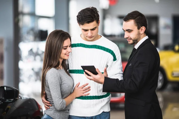 Casal feliz com carro revendedor olhar para tablet em auto show ou salão — Fotografia de Stock