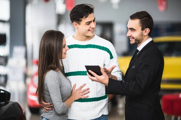 Casal feliz com carro revendedor olhar para tablet em auto show ou salão — Fotografia de Stock