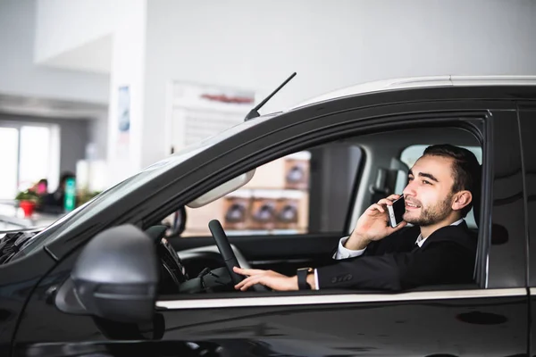Hombre de negocios guapo usando el teléfono inteligente en el coche en la sala de exposición — Foto de Stock